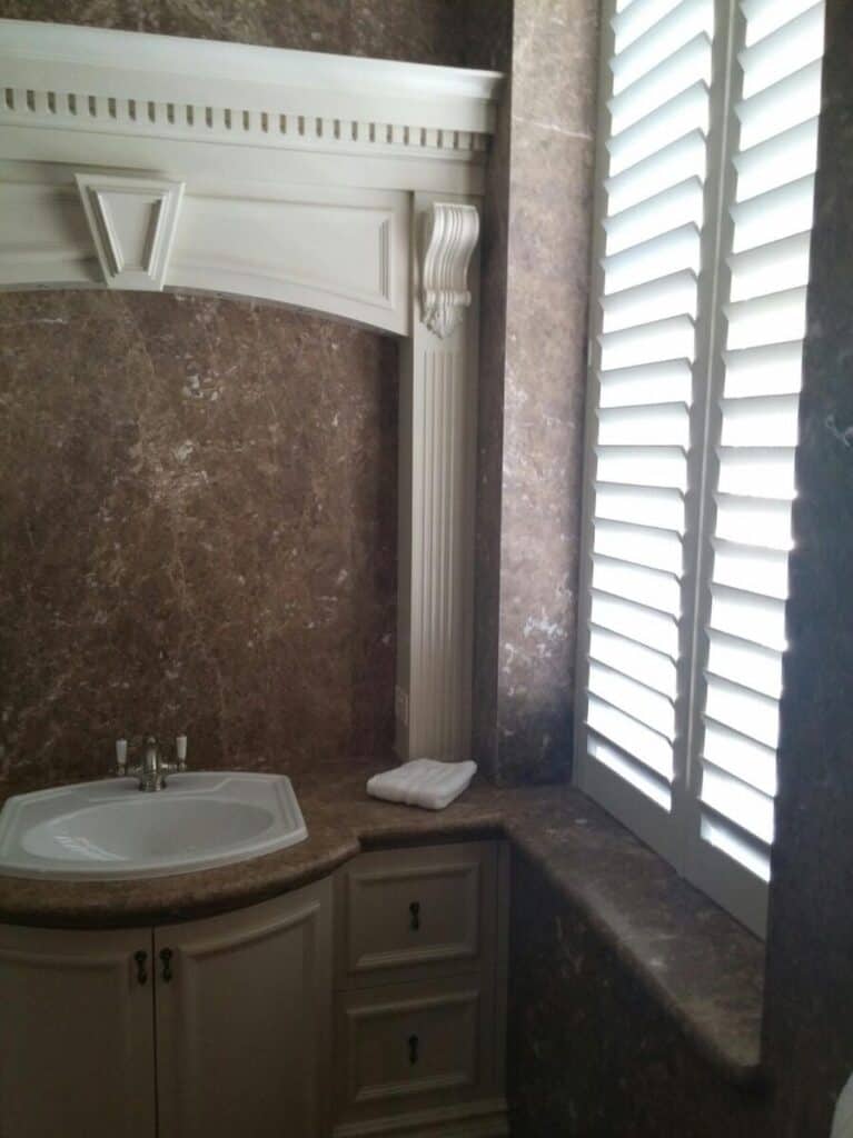 White plantation shutters at a bathroom window in a traditional Perth home, slats tilted for privacy with daylight coming through.